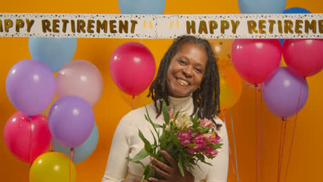 Studioporträt-Einer-Frau-Auf-Einer-Ruhestandsfeier,-Die-Einen-Blumenstrauß-Hält-Und-Mit-Luftballons-Feiert-1